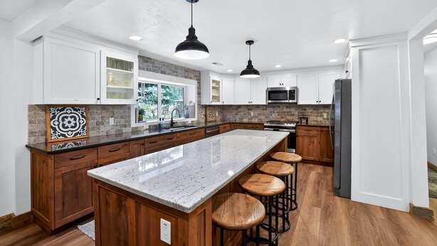 A modern kitchen with a large island, wooden cabinets, and a built-in microwave.