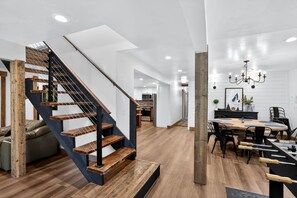 Un interior moderno con una escalera de madera, una zona de comedor con una mesa grande y una cocina al fondo.