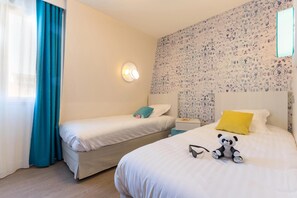 Quarto de hotel com duas camas, uma mesa de cabeceira, uma luminária na parede e um brinquedo de pelúcia com formato de panda.