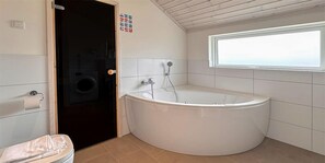 A bathroom with a bathtub, toilet, and a window. - Ferienhaus mit Sauna und Whirlpool in Bad Bevensen (Bad Bevensen)