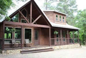 A wooden cabin with a large porch, multiple windows, and a stone foundation. - New Listing Special! Stocked Fishing Pond, Firepit & Kayak Adventure Await! (Broken Bow)