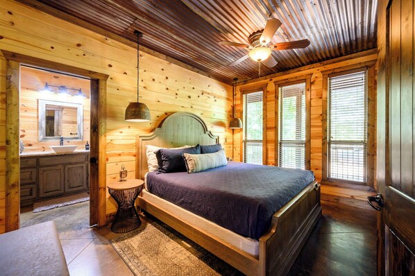 Ein Schlafzimmer einer Holzhütte mit Bett, Nachttisch, Deckenventilator und einem Fenster mit Jalousien.