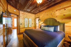 Un dormitori de cabana de fusta amb llit, una tauleta de nit i un ventilador de sostre.