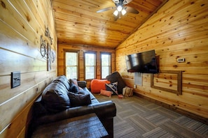 Ein gemütliches Blockhäuschen-Interieur mit einer Ledersofa, einem flachbildfernseher an der Wand und einem Deckenventilator.