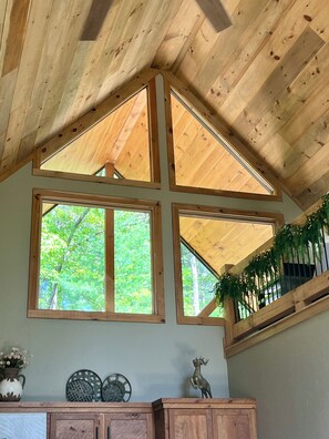 A room with a sloped wooden ceiling, large windows, and a wooden cabinet with decorative items. - Peaceful Retreat in McCaysville Georgia (McCaysville)