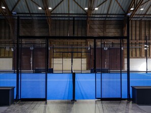 Instalación deportiva con suelo azul, vallas metálicas y estructura de techo de madera.