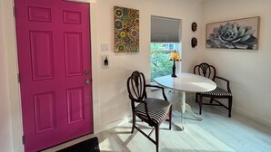 Una habitación con una puerta rosa, una mesa de comedor con sillas, un ventanal con vistas y decoración en la pared.