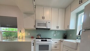 Una cocina moderna con armarios blancos, un microondas, una estufa y un cubo de basura.