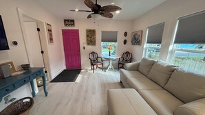 Una sala de estar con un sofá blanco, una mesa azul, una puerta rosa y un ventilador de techo.