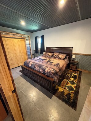 A bedroom with a wooden bed, a nightstand, a dresser, and a window with curtains.