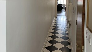 Ein Hotelgang mit Schachbrettfußboden, weißen Wänden und gerahmten Kunstwerken.