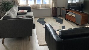 Ein stilvolles Wohnzimmer mit Sofa, Fernsehtisch und großem Fenster mit Vorhängen.