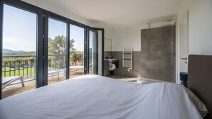 Quarto com uma cama grande, banheiro com chuveiro e varanda com vista.