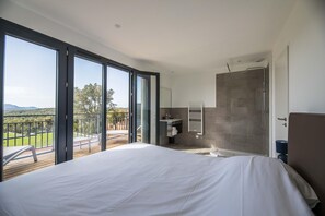 Une chambre avec un grand lit, une salle de bain avec douche et un balcon avec vue.