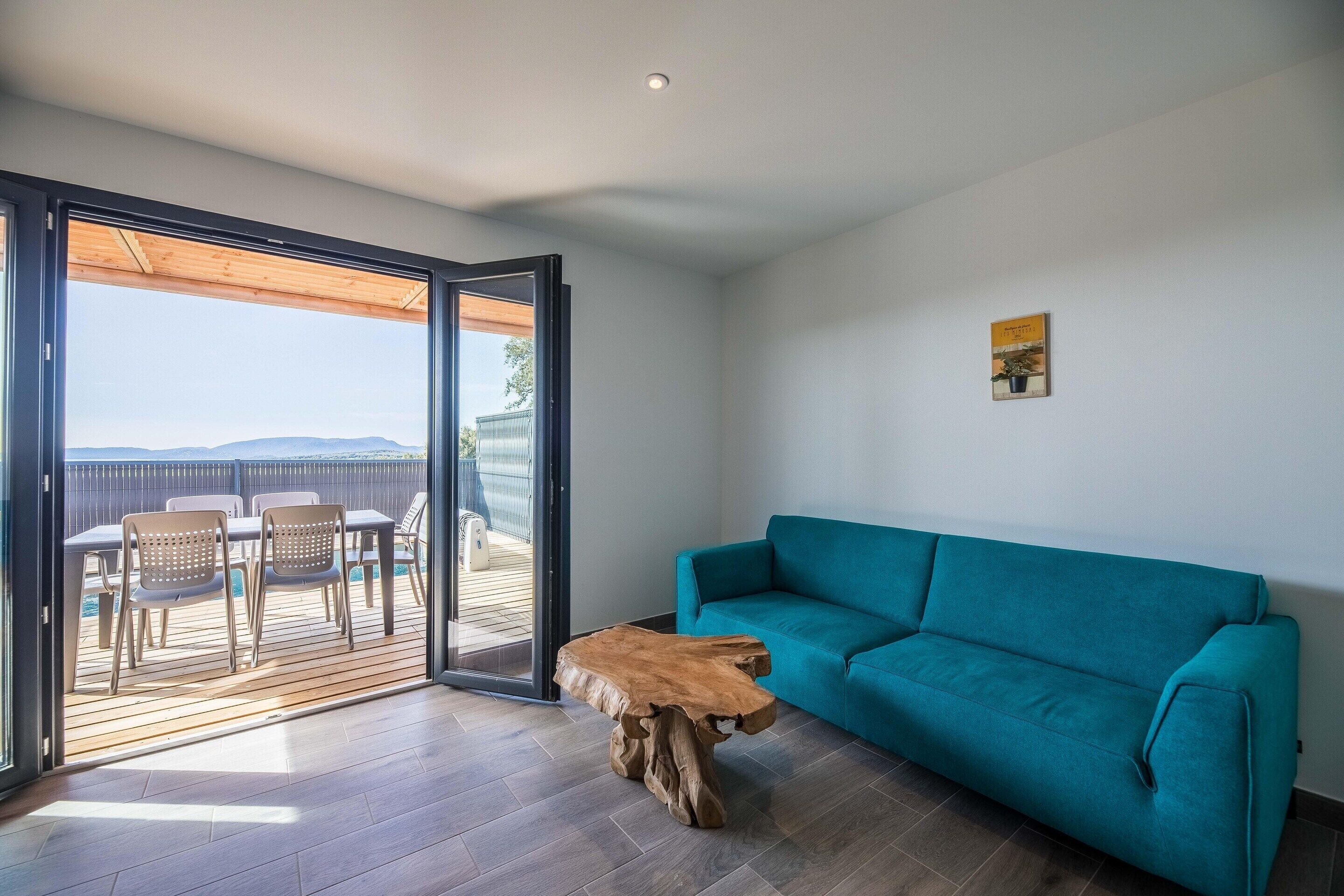 An interior with a sofa, a wooden coffee table, and a view through a sliding door to an outdoor deck.