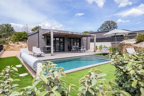 Una casa moderna con piscina, mobiliario exterior y una pérgola.
