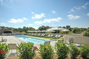 A pool area with lounge chairs and umbrellas, surrounded by greenery and a clear sky. - Sun-drenched Corsican Flat (Lecci)