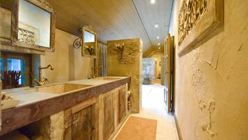 Un baño con tocador de madera, un espejo grande y una pared decorativa de piedra.