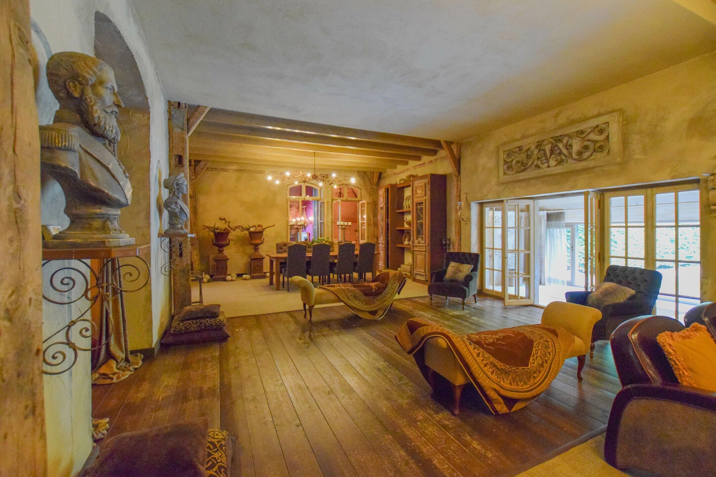 A spacious room with wooden flooring, a dining area with chairs and a table, and a large window with a view.
