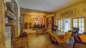 A spacious room with wooden flooring, a dining area with chairs and a table, and a large window with a view.