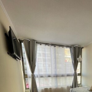 Ein Hotelzimmer mit Bett, Wandfernseher und einem Vorhangfenster.