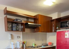 Eine Küche mit Holzausstattung, einer Mikrowelle, einem roten Kühlschrank und einem Regal mit Weingläsern und einer mit 'Oster' beschrifteten Kiste.