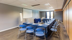 Ein Konferenzraum mit einem langen Tisch, Stühlen, einer Projektionsleinwand und einem Fenster.