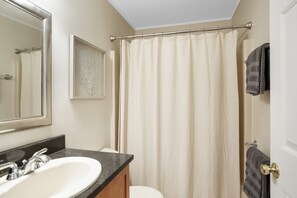 A bathroom with a sink, mirror, shower curtain, towel rack, and a framed picture on the wall.