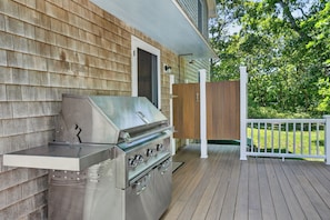 Un barbecue en acier inoxydable sur une terrasse en bois, avec une balustrade blanche et une clôture en bois en arrière-plan.
