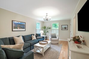 A living room with a sofa, armchair, coffee table, and a chandelier.