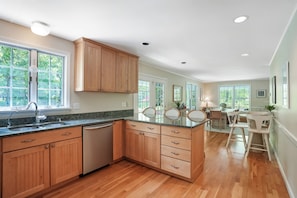A kitchen with wooden cabinets, a dishwasher, and a dining area with chairs and a table.