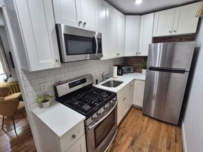 A modern kitchen with white cabinets, stainless steel appliances, and a wooden floor. - Elegant 1-bedroom apt. in a Classic Brooklyn Brownstone with private backyard (Brooklyn)