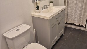 Et badeværelse med toilet, håndvask, spejl og bruseforhæng.