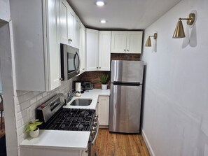 A compact kitchen with white cabinets, a stainless steel refrigerator, a microwave, a gas stove, and a sink.
