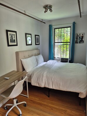 A bedroom with a bed, a desk, and a chair. There are framed pictures on the wall and a window with curtains. - Elegant 1-bedroom apt. in a Classic Brooklyn Brownstone with private backyard (Brooklyn)