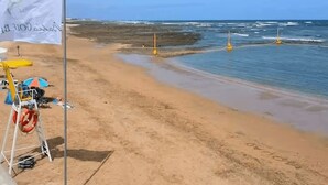 Une plage avec un drapeau, une bouée de sauvetage et une chaise jaune.