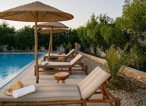 A poolside area with lounge chairs, wooden tables, and thatched umbrellas.