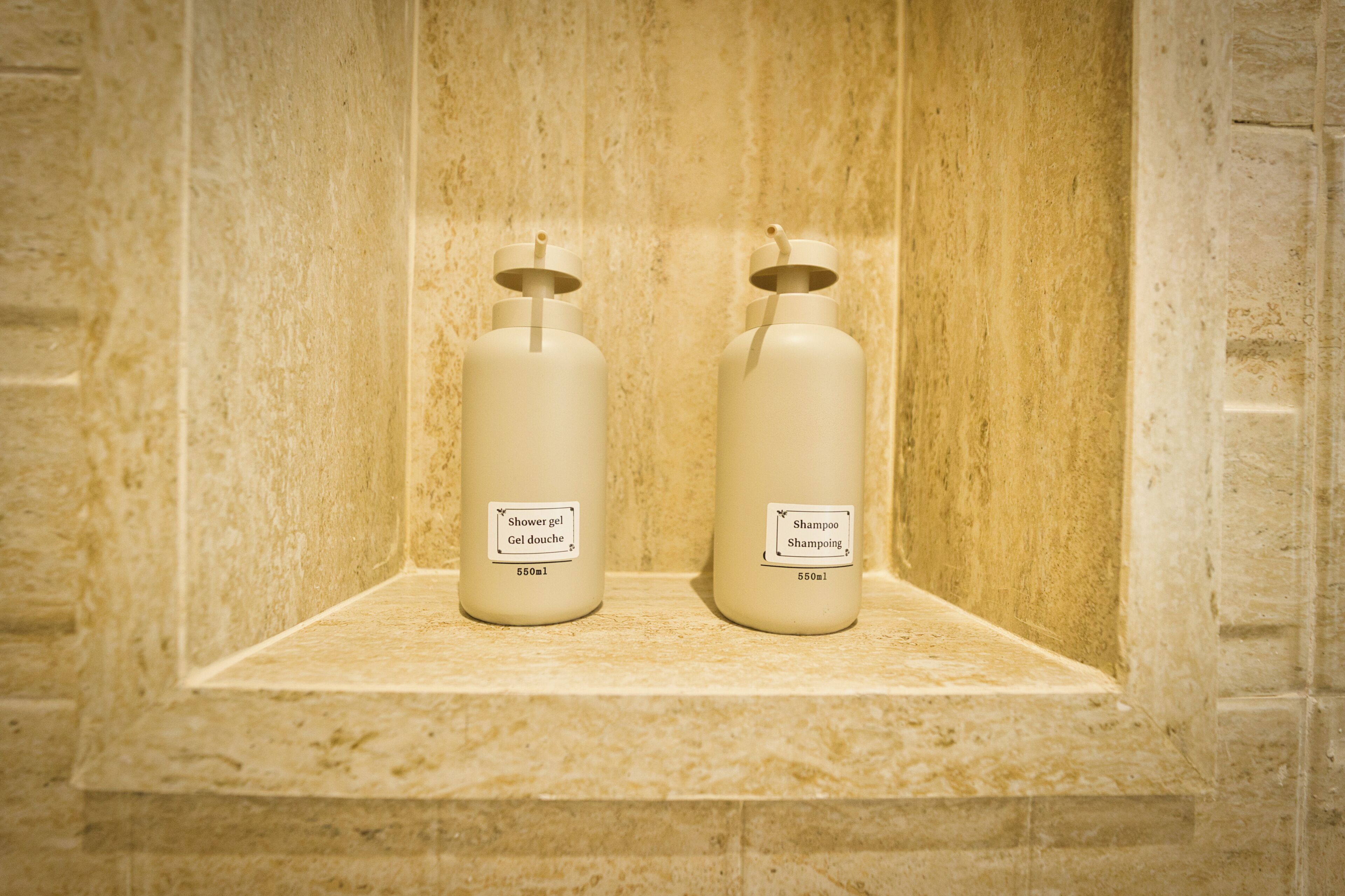 Deux bouteilles de gel douche et de shampoing sur une étagère en marbre.