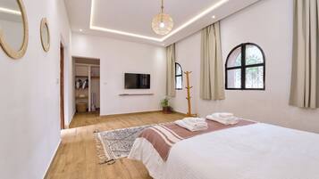 Une chambre moderne avec un grand lit, un téléviseur à écran plat, un plancher en bois et une fenêtre avec des rideaux.