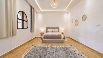 Une chambre à coucher avec un lit, des lampes de chevet, un luminaire suspendu, une fenêtre avec des rideaux et un tapis à motifs.