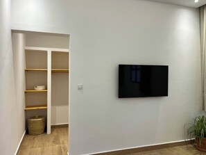 Moderni huone, jossa on seinälle asennettu taulutelevisio, puuhyllyt ja lattialla punottu kori.