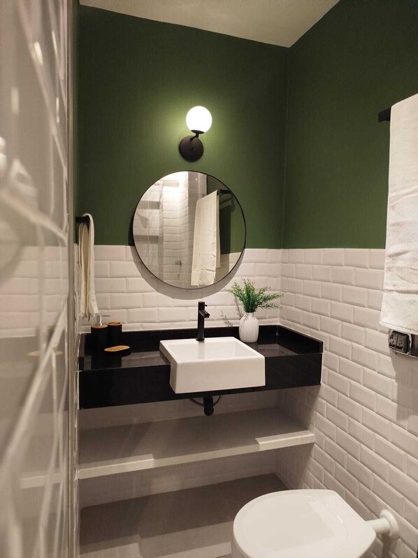 A bathroom with a white sink, black countertop, and a round mirror. - Covivere - Humaitá - RJ (Rio de Janeiro)