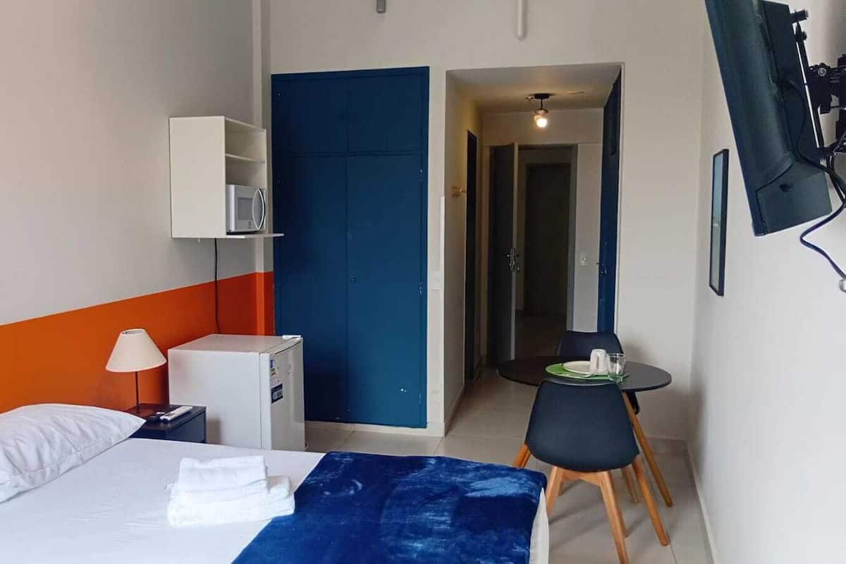 Une chambre dâhĂŽtel Ă©quipĂ©e dâun lit, dâun bureau, dâune chaise, dâun four Ă micro-ondes et dâun petit rĂ©frigĂ©rateur, ainsi que dâune porte donnant sur une autre piĂšce.