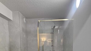 Un baño moderno con ducha de mampara de vidrio, inodoro y lavamanos.