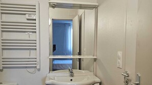 Un baño con lavamanos, espejo e inodoro blancos.