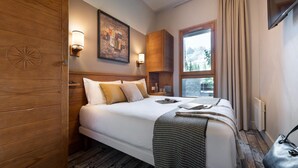 A hotel room with a wooden headboard, a large bed with white linens, a painting on the wall, and a window with a view of trees. - Scenic 4-person Mountain View Retreat (Araches-la-Frasse)