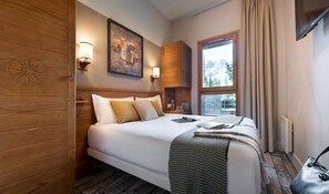 Ein Hotelzimmer mit Holz-Kopfteil, einem großen Bett mit weißen Leinen, einem Bild an der Wand und einem Fenster mit Blick auf Bäume.