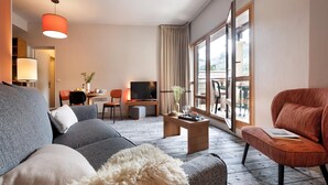 A modern hotel room with a grey sofa, a red armchair, a wooden coffee table, a TV, and a dining area with a table and chairs. - Scenic 4-person Mountain View Retreat (Araches-la-Frasse)