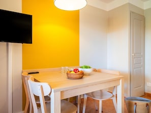 A dining area with a wooden table, white chairs, a bowl of salad, and a basket of fruit.