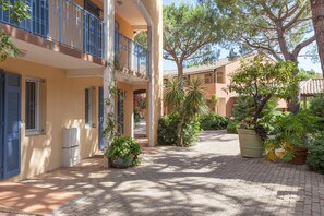 Un patio con un camino de baldosas, plantas en macetas y un edificio con balcones.